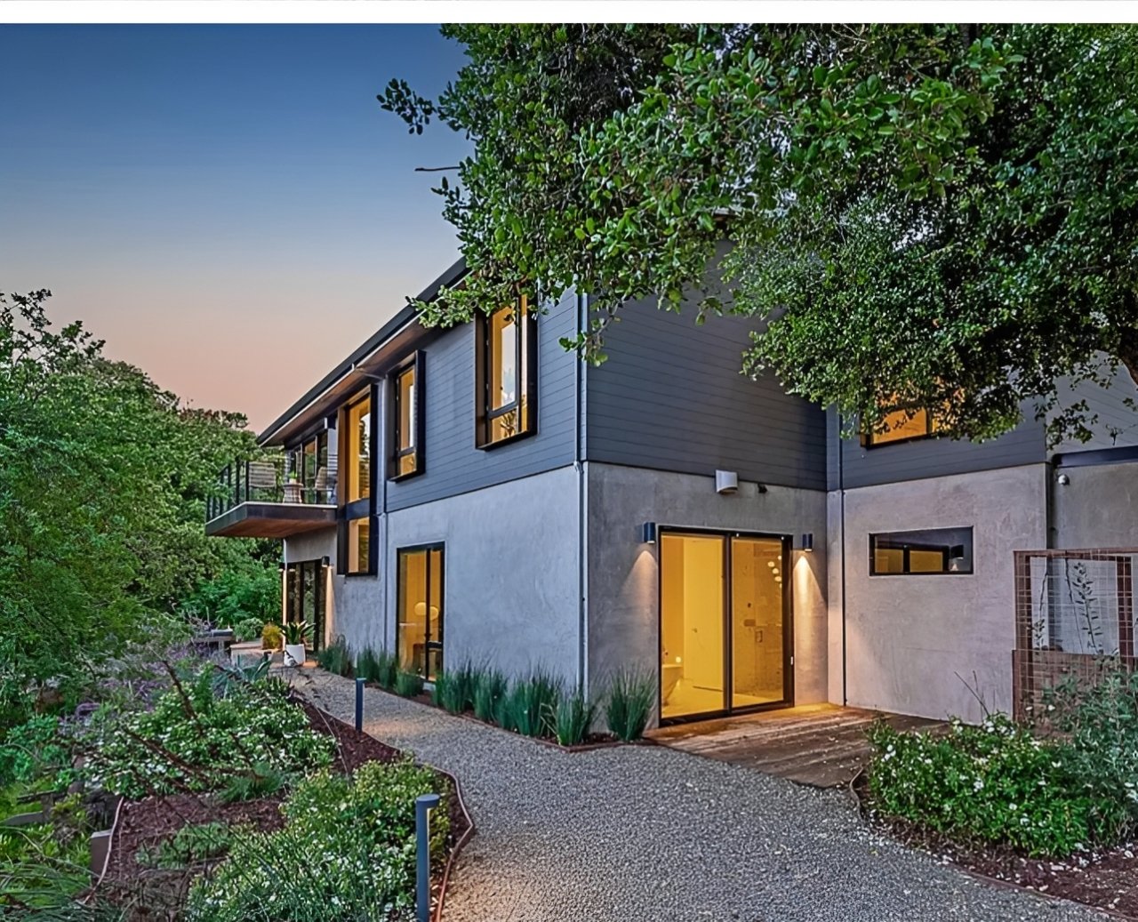 Two-story modern home with concrete base and lit gravel path